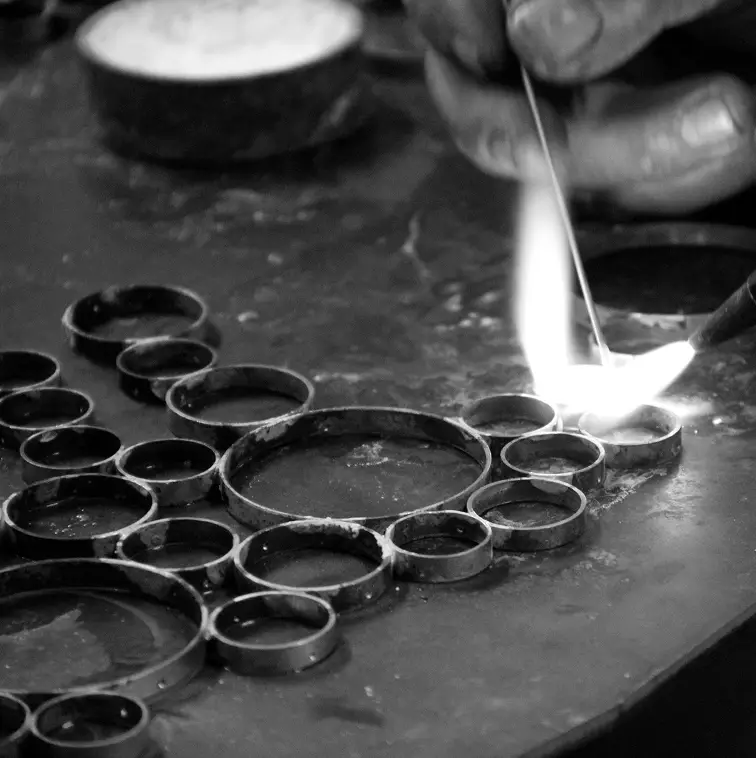 A person's hand soldering metal rings together, showcasing Koket's metallic crafting.