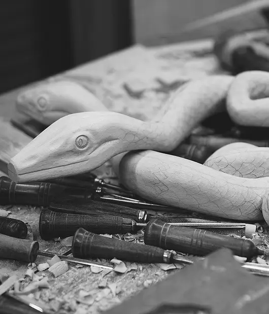 A grayscale close-up of a carved wooden serpent sculpture, showcasing intricate details and craftsmanship.