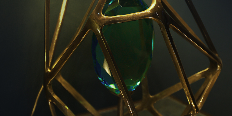 Close-up of a green faceted Gem Table Lamp encased in a gold geometric metal frame.