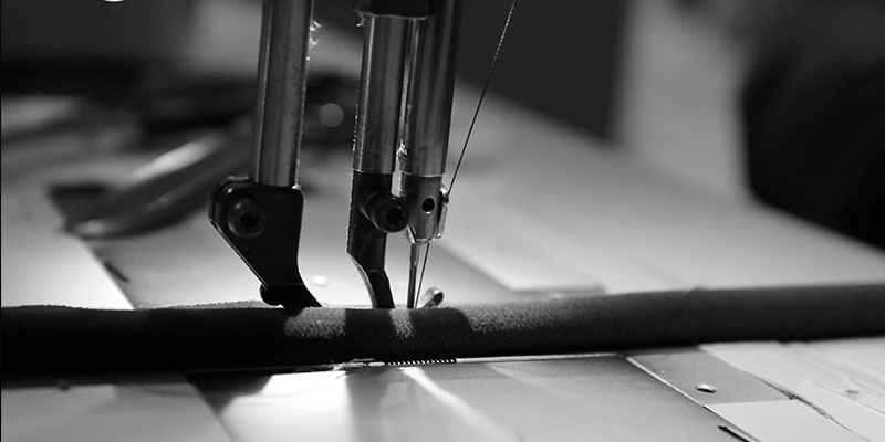 Close-up, black and white shot of a sewing machine needle working on the upholstery for the Chandra Chair.