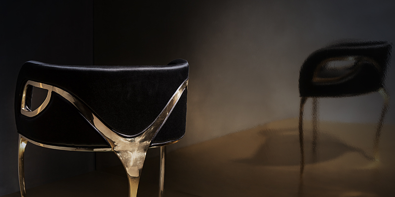 Elegant black Koket Chandra Chair with polished brass details, set against a dark background with a reflective surface.