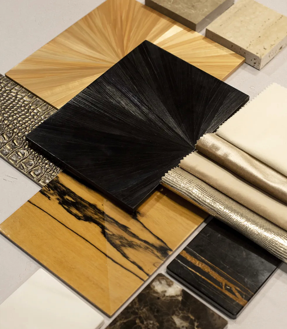A variety of luxurious material samples for furniture, including textured wood panels, a crocodile-embossed leather, and various rolls of elegant fabrics.