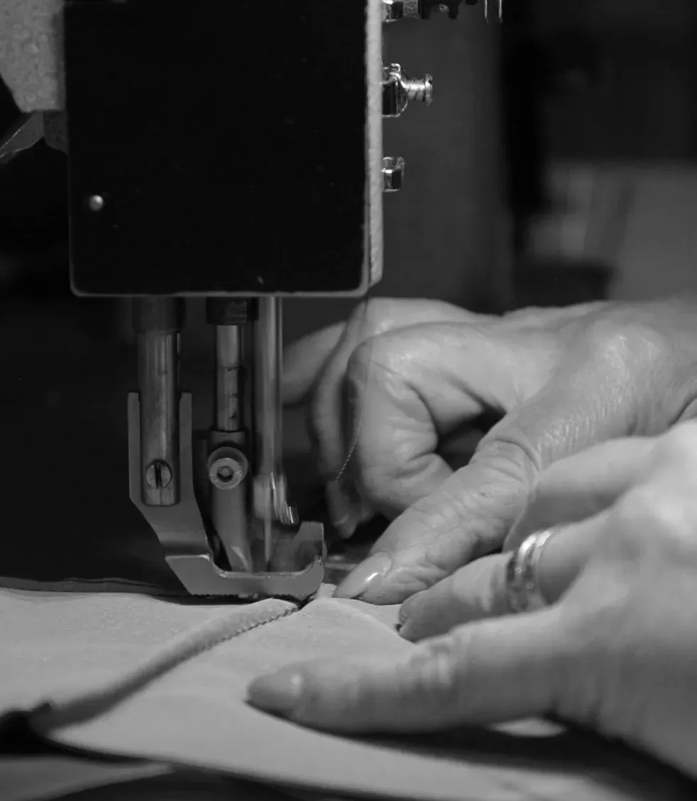 Close-up of a person's hands guiding fabric through an industrial sewing machine, stitching a seam with precision.