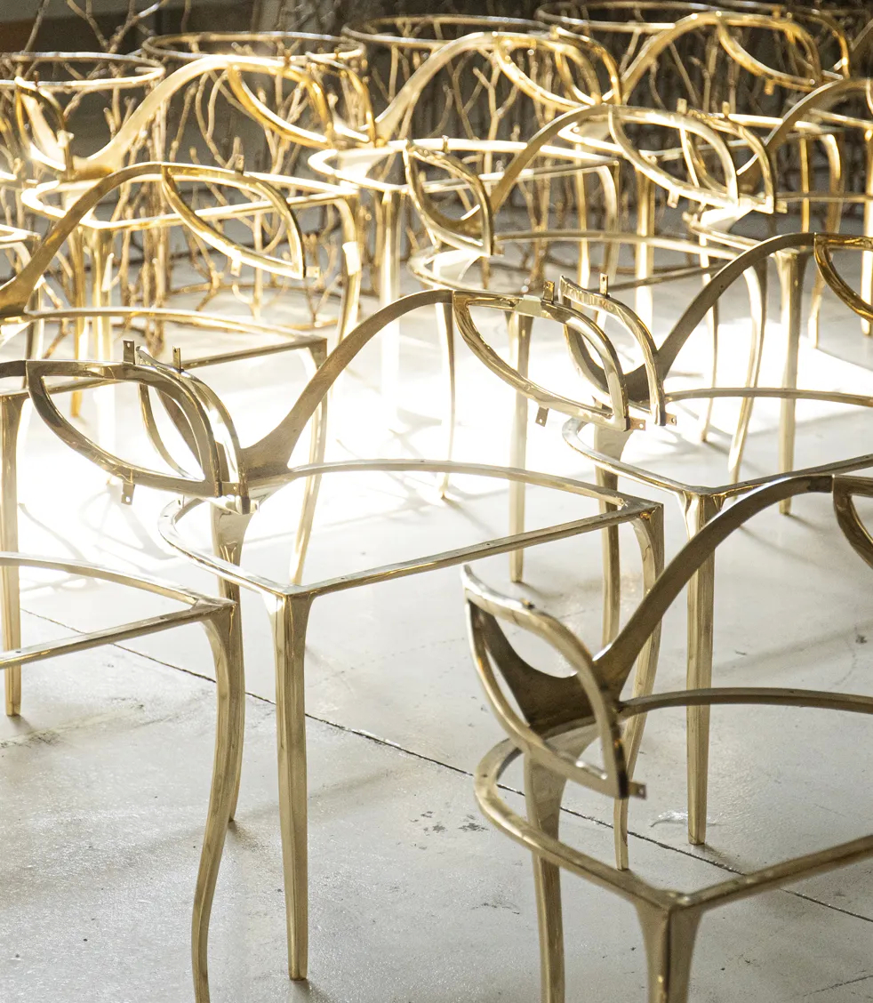 A factory floor is filled with numerous intricate, golden metal frames for luxury furniture pieces, arranged closely together.