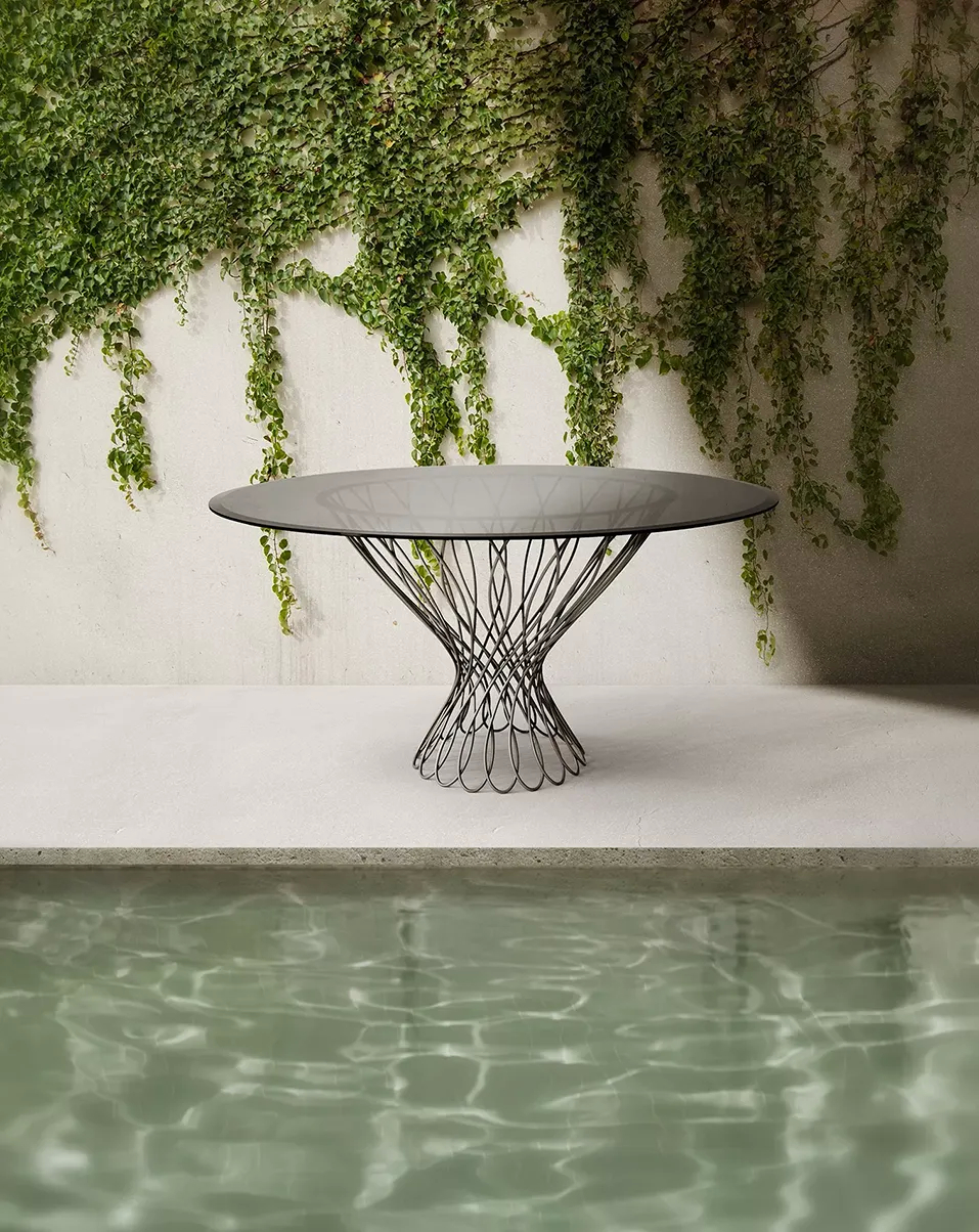 A contemporary outdoor space features the Allure Dining Table by Koket next to a pool, against a green ivy wall.