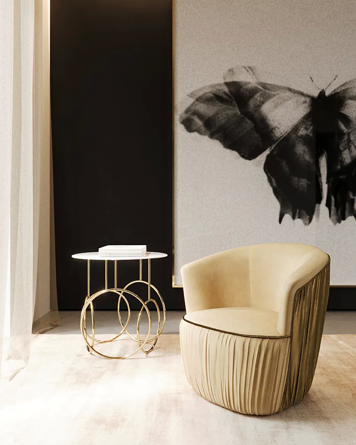A cream Countess Chair with pleated details and a gold Kiki Side Table with a white top, against a black wall with butterfly art.