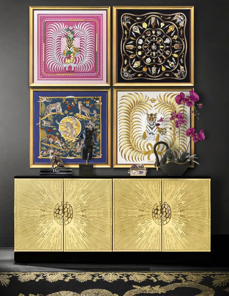 A luxurious gold Heive Cabinet with sunburst doors under four framed, colorful, patterned artworks on a dark wall.
