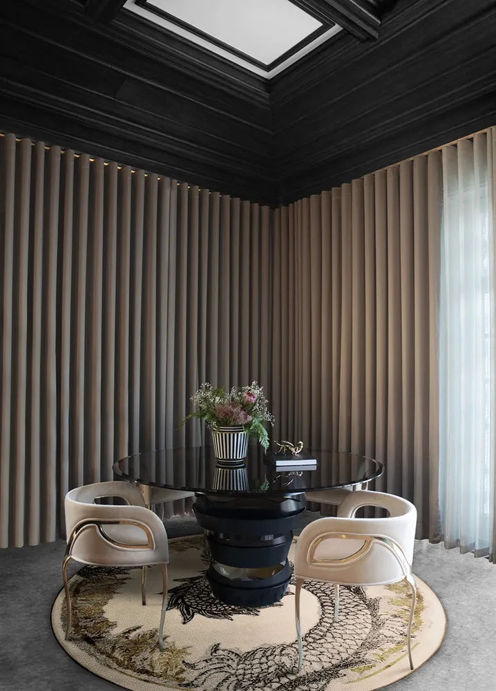 A lavish dining room features a KOKET Intuition Dining Table with a metallic base and several black Chandra Chairs.