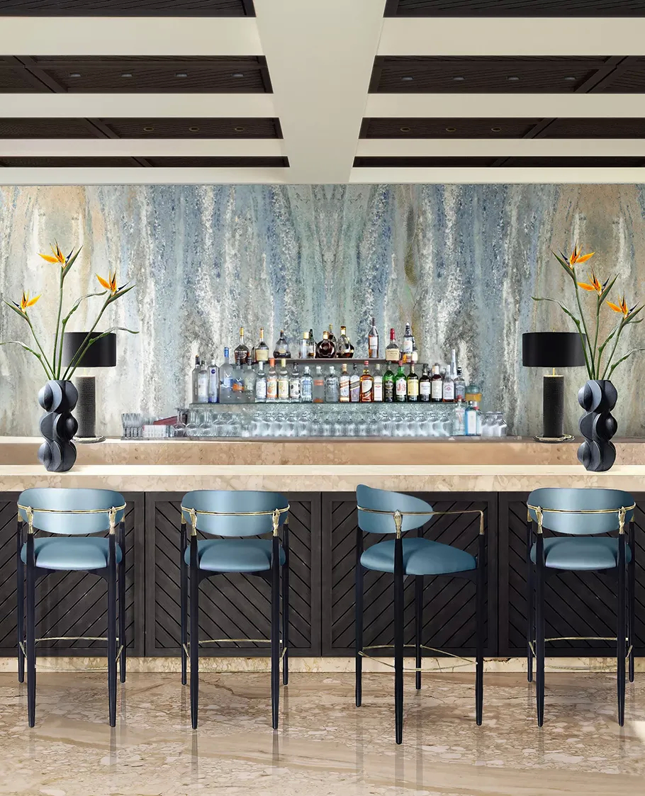 Four Nahéma Bar Stools by Koket with blue seats line a long bar with a mirrored back and a textured blue wall.