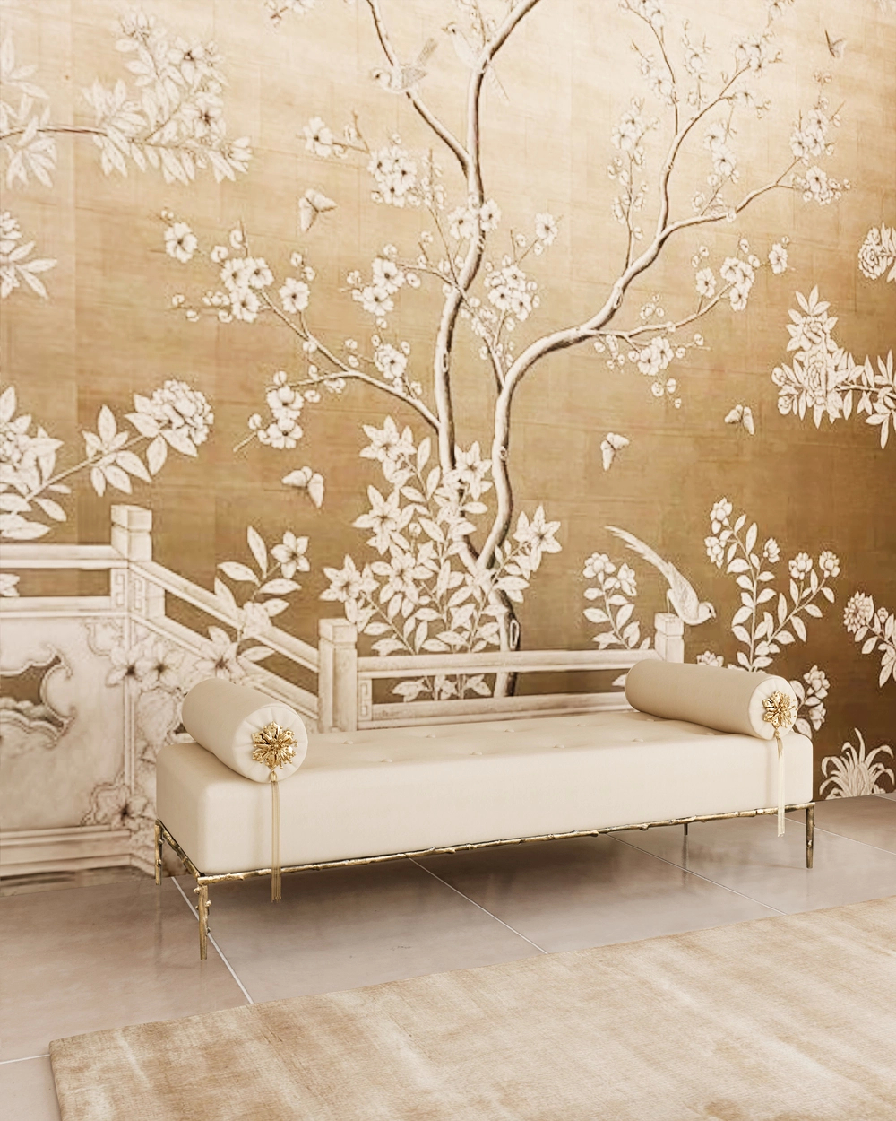 An elegant Privê Bench, upholstered in cream fabric with gold legs and two cream bolsters with gold tassel ends, sits on a light rug in front of a stunning gold wall mural featuring white cherry blossoms, birds, and butterflies.