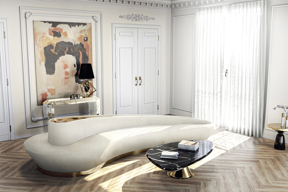 A luxurious, cream-colored curved Reptilia sofa with a gold base in a modern, elegant living room.