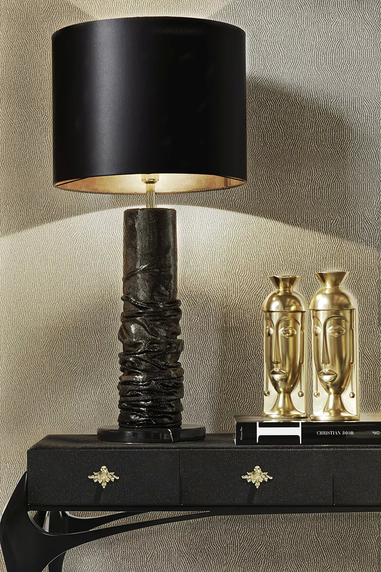 A stylish black Ruchê Table Lamp by Koket with a black shade and two gold decorative vases on a black console table.
