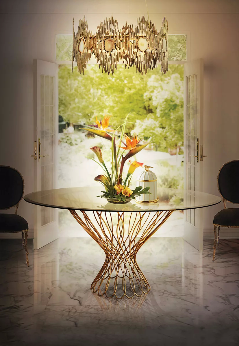 With the light of an open door in the background, leading to the nature, this dining room has a graceful Allure Dining Table with its silhouette shaped golden structure with two black Enchanted Chairs next to it. Above it there is the Vivre Chandelier, in golden hues and with agate stones incorporated, bringing a vintage vibe into the room.