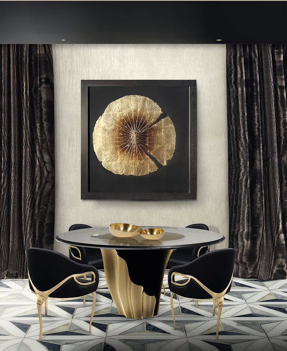 This dining room is a study in dramatic elegance, where dark sophistication meets the luminous glow of gold. The centerpiece is Yasmine, a round dining table, with a smoked tabletop, resting upon a sculptural golden and black base, capturing the room’s bold yet refined essence. Surrounding the Yasmine table, sleek black Chandra chairs with curved golden frames echo the table's luxurious form, their soft silhouettes, with the distinctive characteristic of having 3