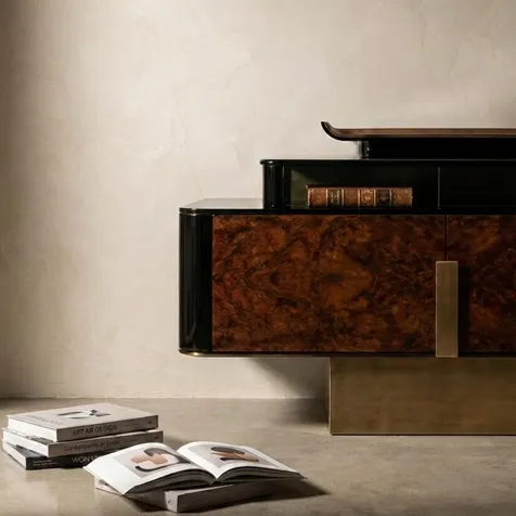 KOKET Women Art Deco luxury chest with rich wood veneer doors, black lacquer frame, gold base and styled art books in an elegant interior.