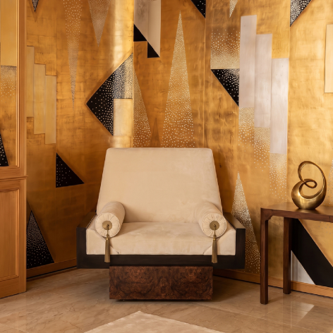 KOKET Lola armchair in cream upholstery with dark wood frame, front view against a sculptural gold geometric wall.