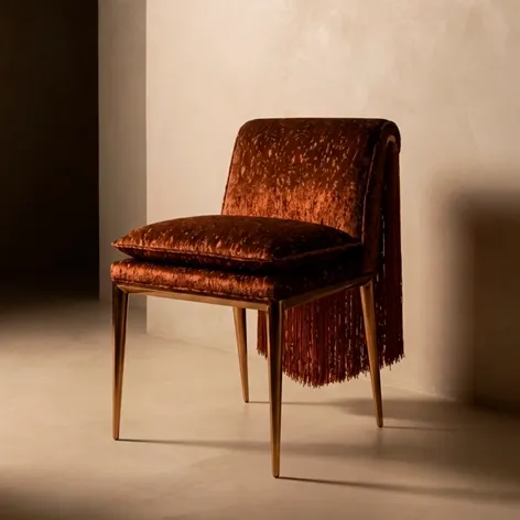 KOKET Women Art Deco luxury chair with brown velvet upholstery, cascading fringe back and slender gold legs in a warm interior.