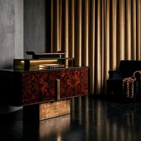 KOKET Women Art Deco luxury chest with rich wood veneer doors, black lacquer body and brushed gold pedestal, styled against dramatic drapery.