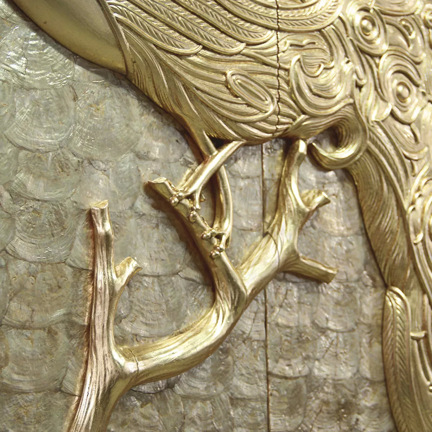 A close-up of the Camilia Mother of Pearl Armoire, showing the intricate details of the gold peacock's feathers and branch.