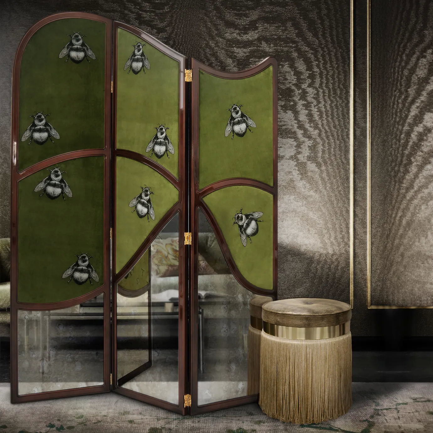 Elegant corner with the Simone screen in green velvet with embroidered bee details and mirror at the bottom, framed by a curved dark structure with golden hinges, next to a beige Amaretto ottoman with golden details and fringes, on a patterned rug, against a dark textured wall.