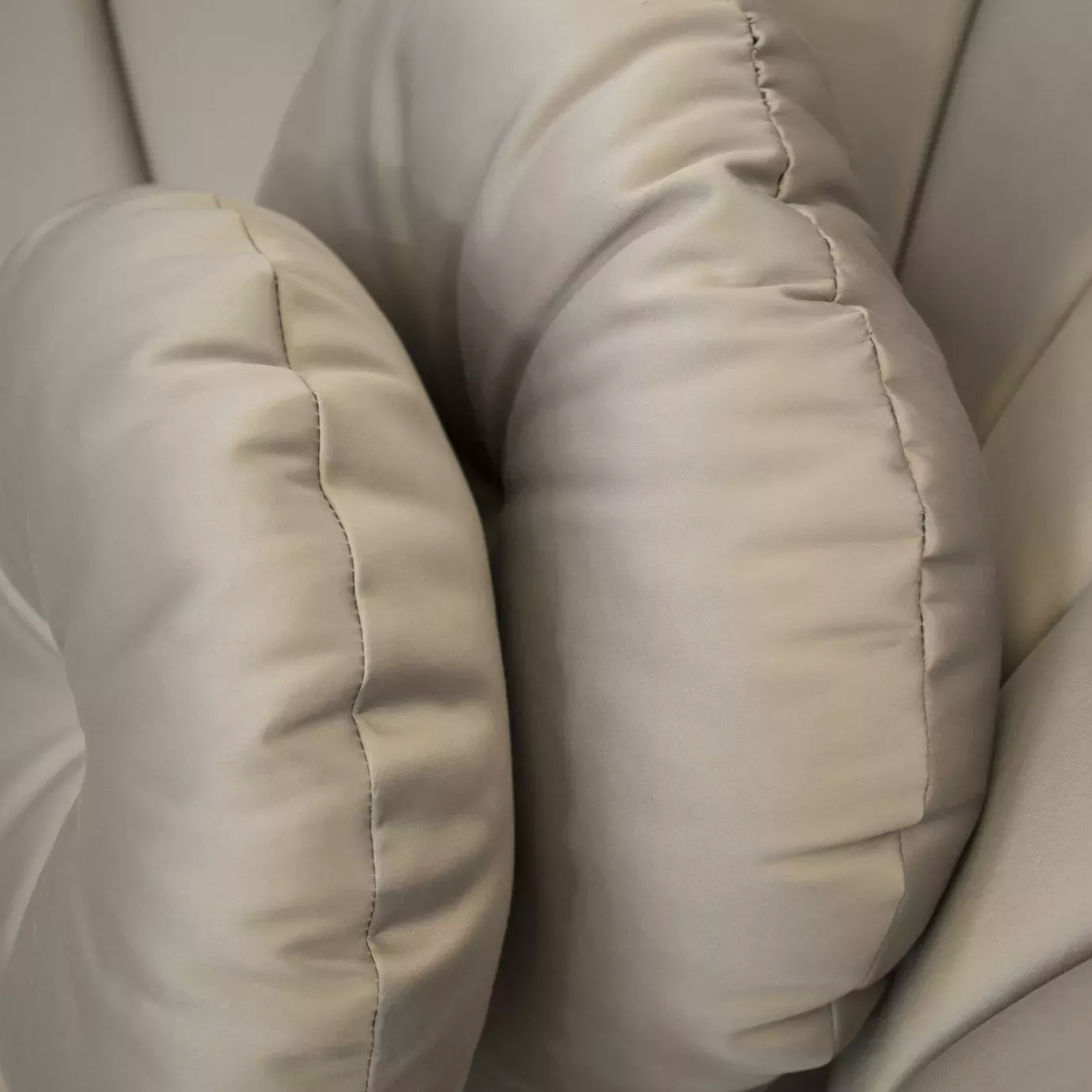 Elegant close-up of the textured details and stitching of a round cushion and the soft beige fabric upholstered arm of the Caprichosa Sofa.