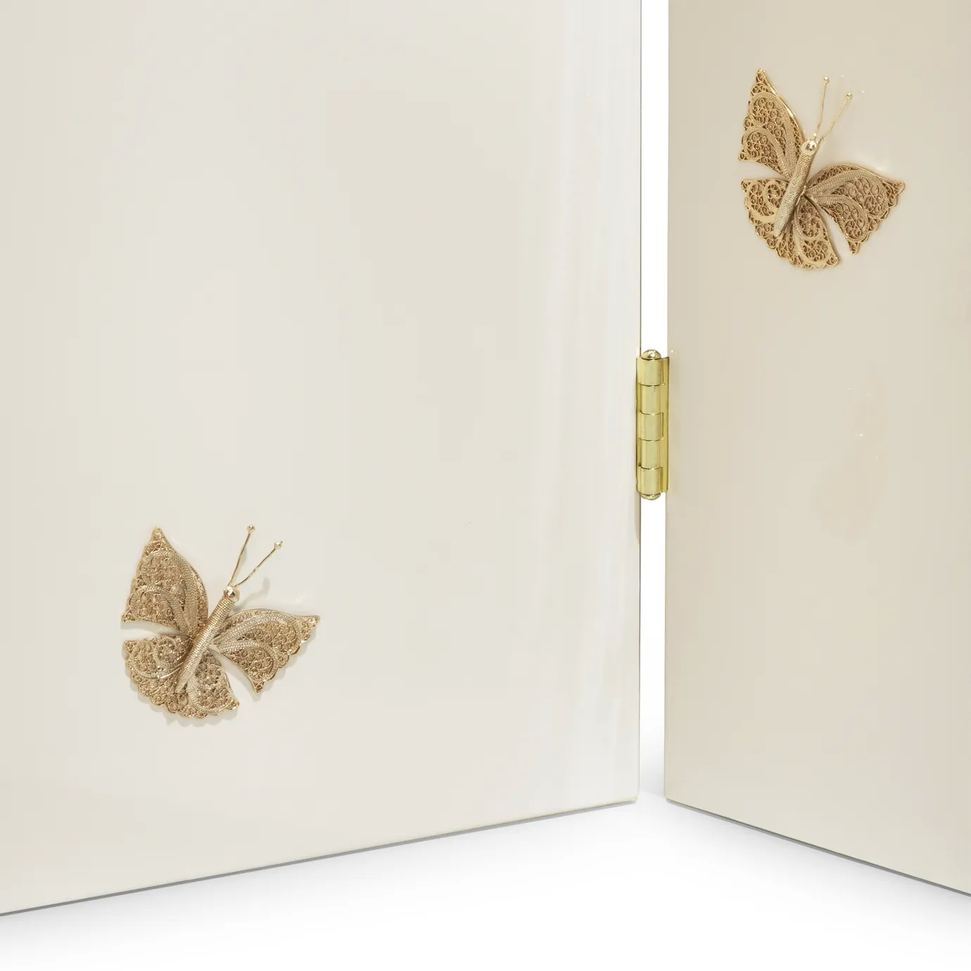 Macro view of the KOKET Euphoria Screen butterfly ornament, a handcrafted filigree piece in gold over a glossy cream backdrop.