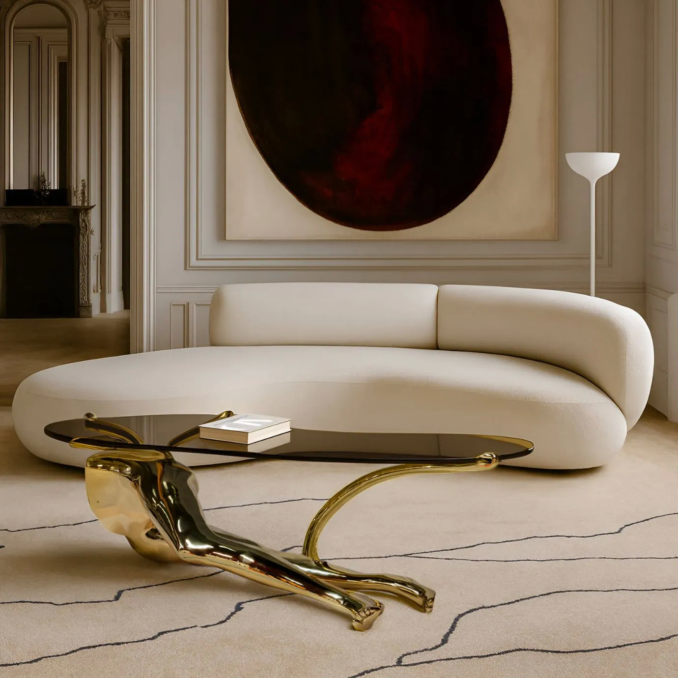 Contemporary living room featuring KOKET’s Tabu Coffee Table with a sculptural gold base and glass top, styled with a curved white sofa, abstract wall art, and neutral tones—an iconic and highly desired luxury furniture piece.