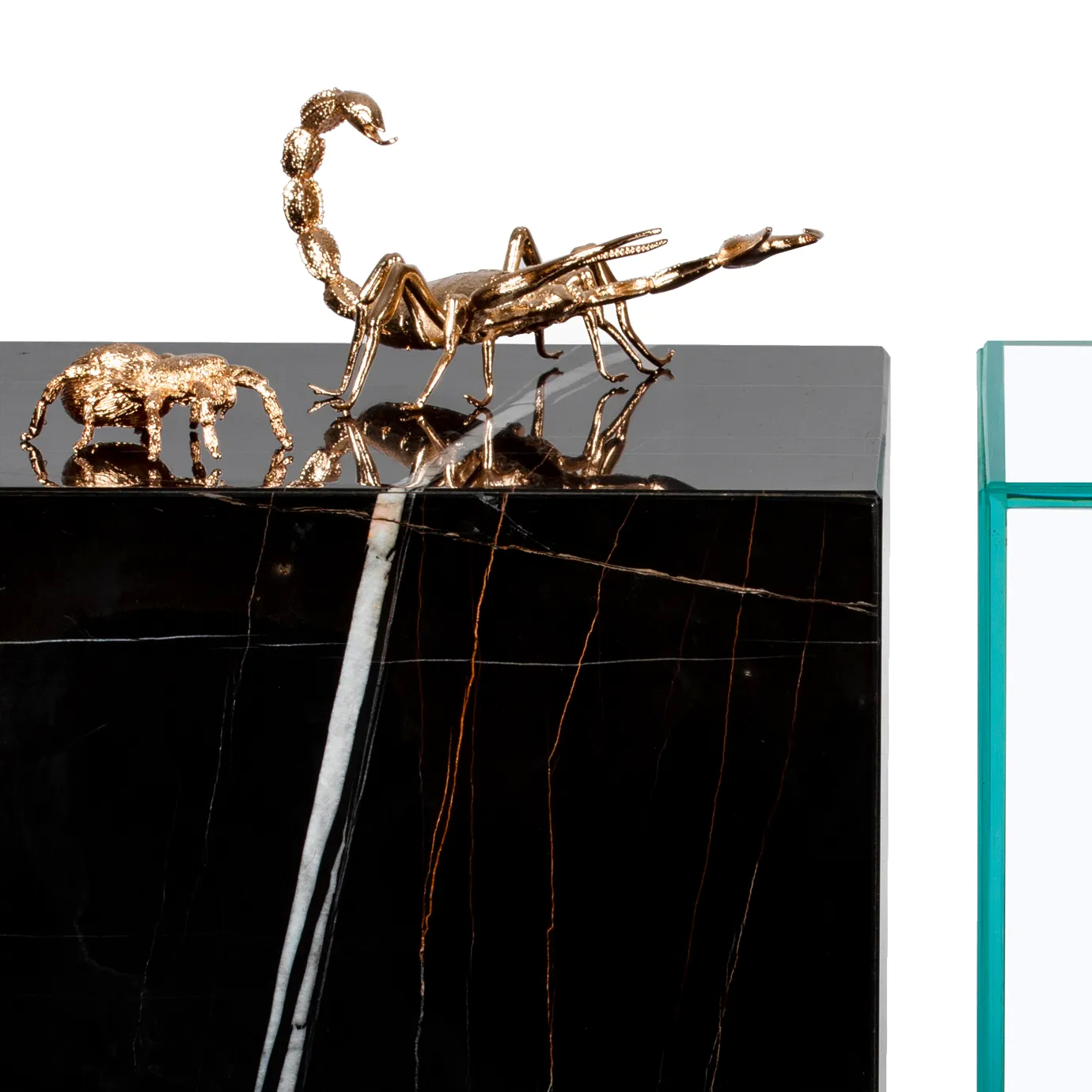Gold scorpion and elephant sculptures on a black marble base, paired with a glass display case.