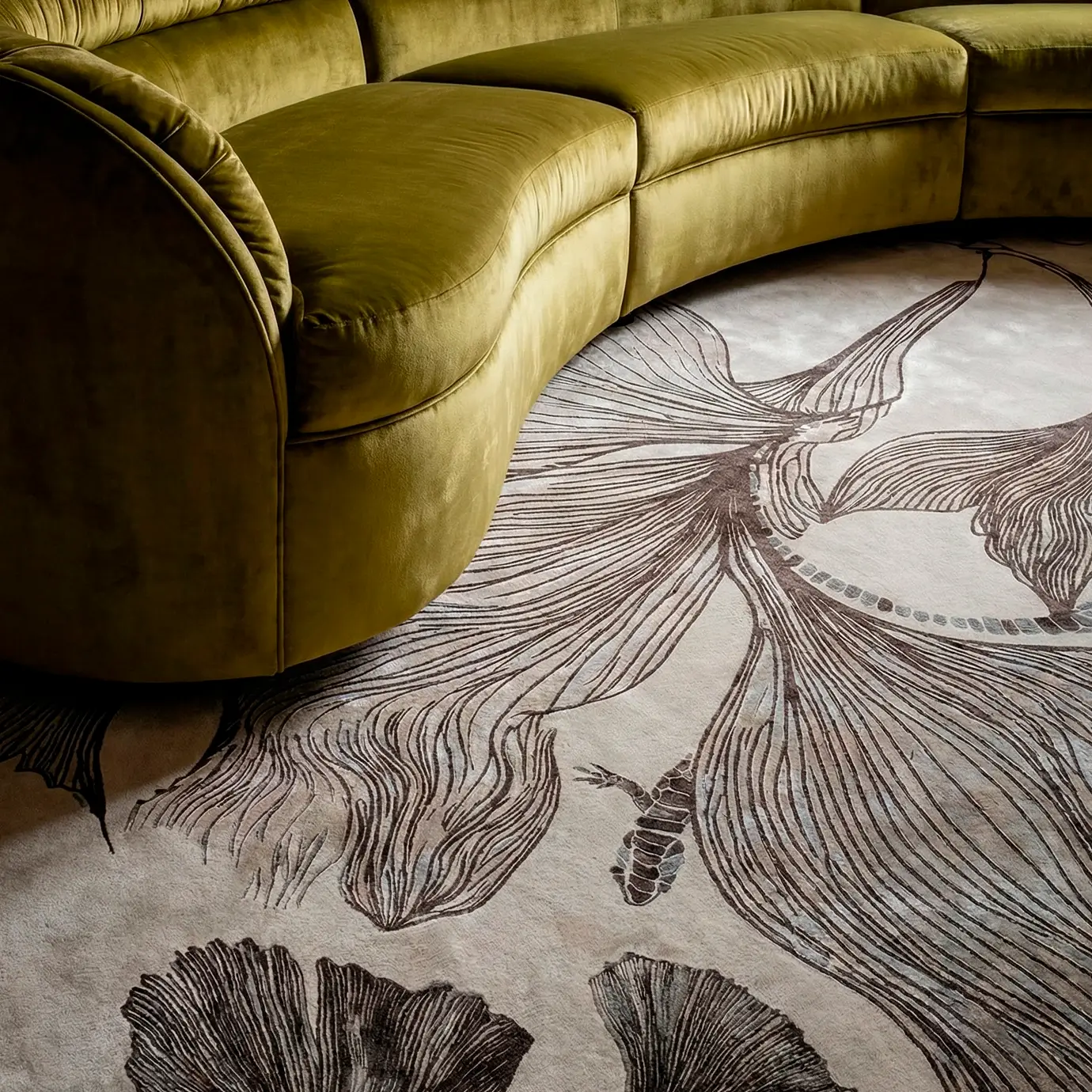 "Luxury living room setting featuring a curved green velvet sofa paired with the KOKET Flora rug. High-end interior design inspiration with designer furniture and premium area rugs.