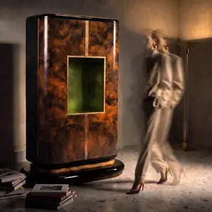 Eleanor armoire by KOKET in a dark interior with a person walking past, books on the floor and the green niche lit.