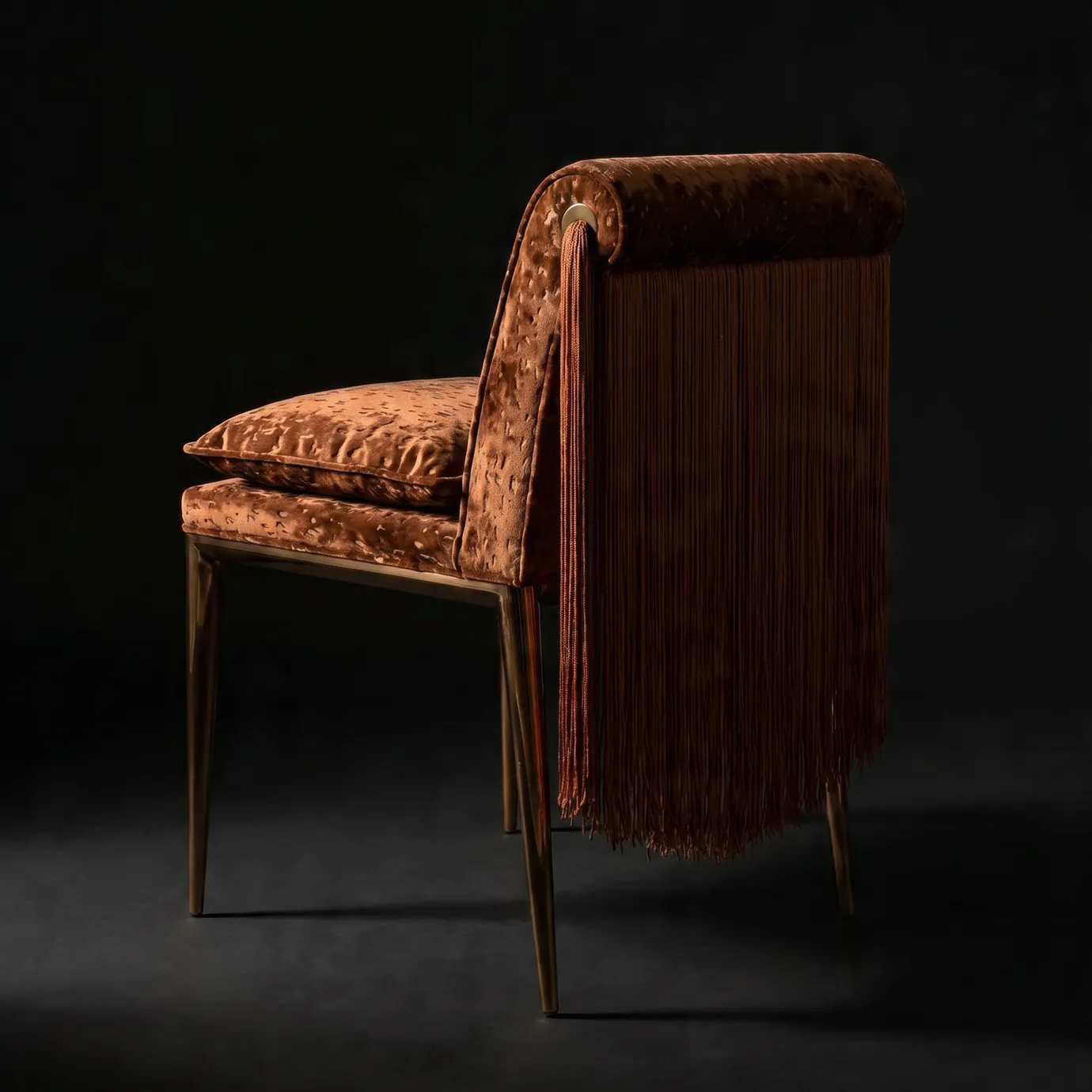 Lucienne dining chair by KOKET seen from the side in a dark interior, highlighting the cascading fringe and brass tassel.