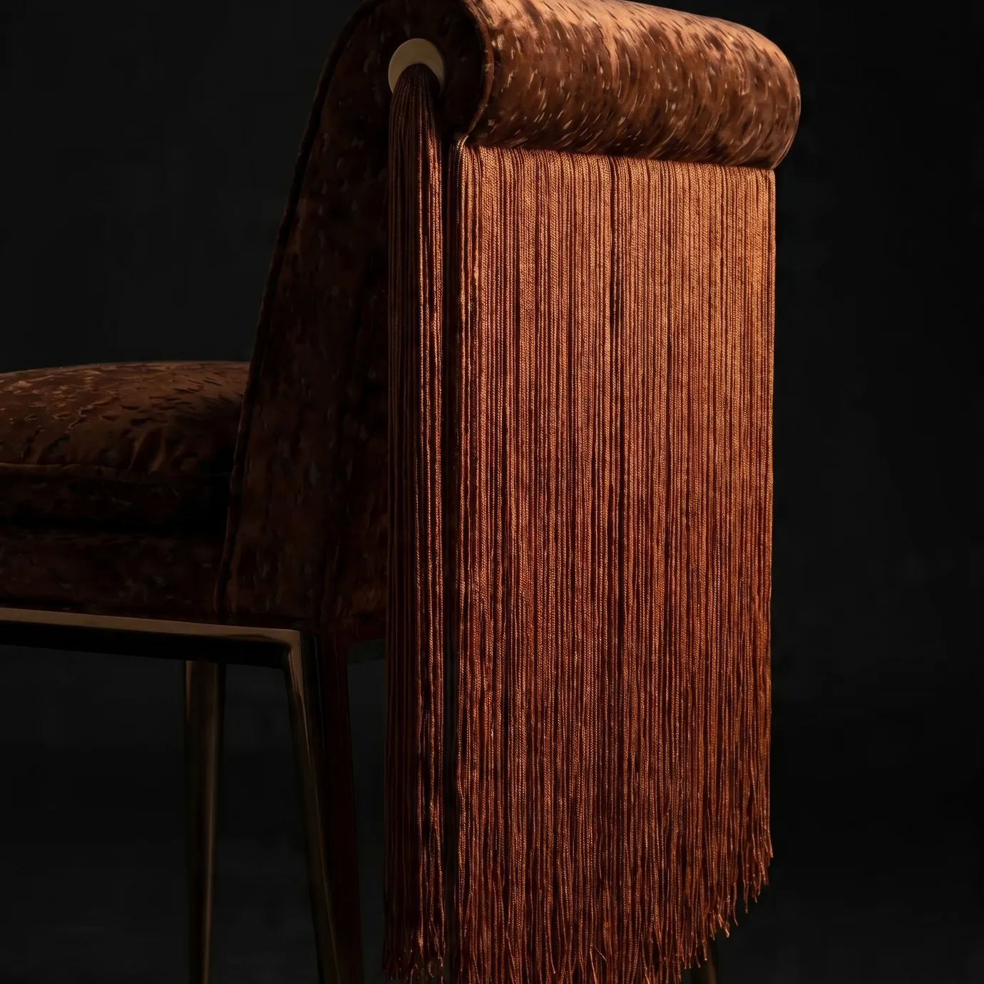 Detail of the rolled back, brass eyelet and tassel on Lucienne dining chair by KOKET above the cascading fringe.