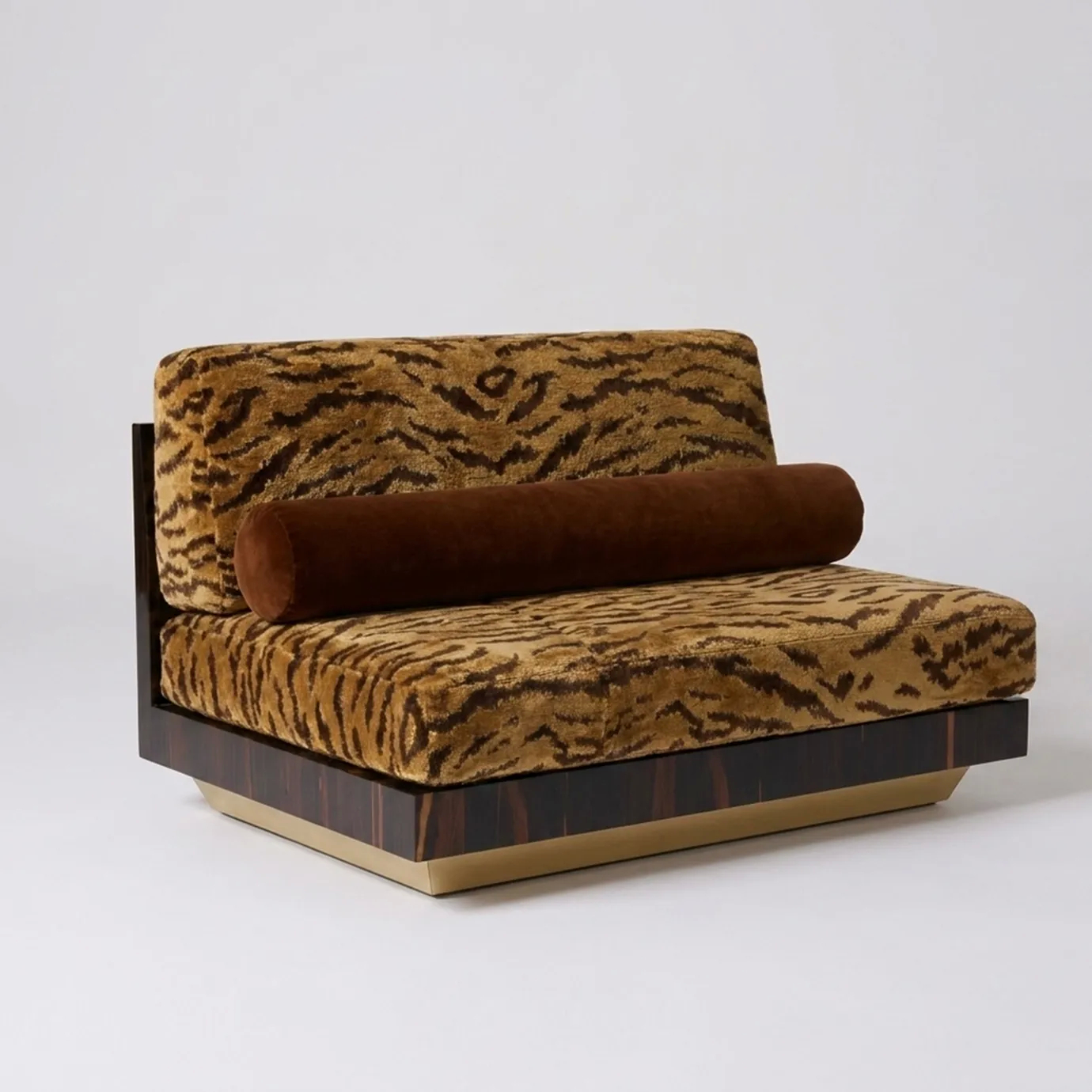 KOKET Women Art Deco luxury sofa with tiger-pattern upholstery, cylindrical bolster cushion and dark wood veneer base with brass detail.