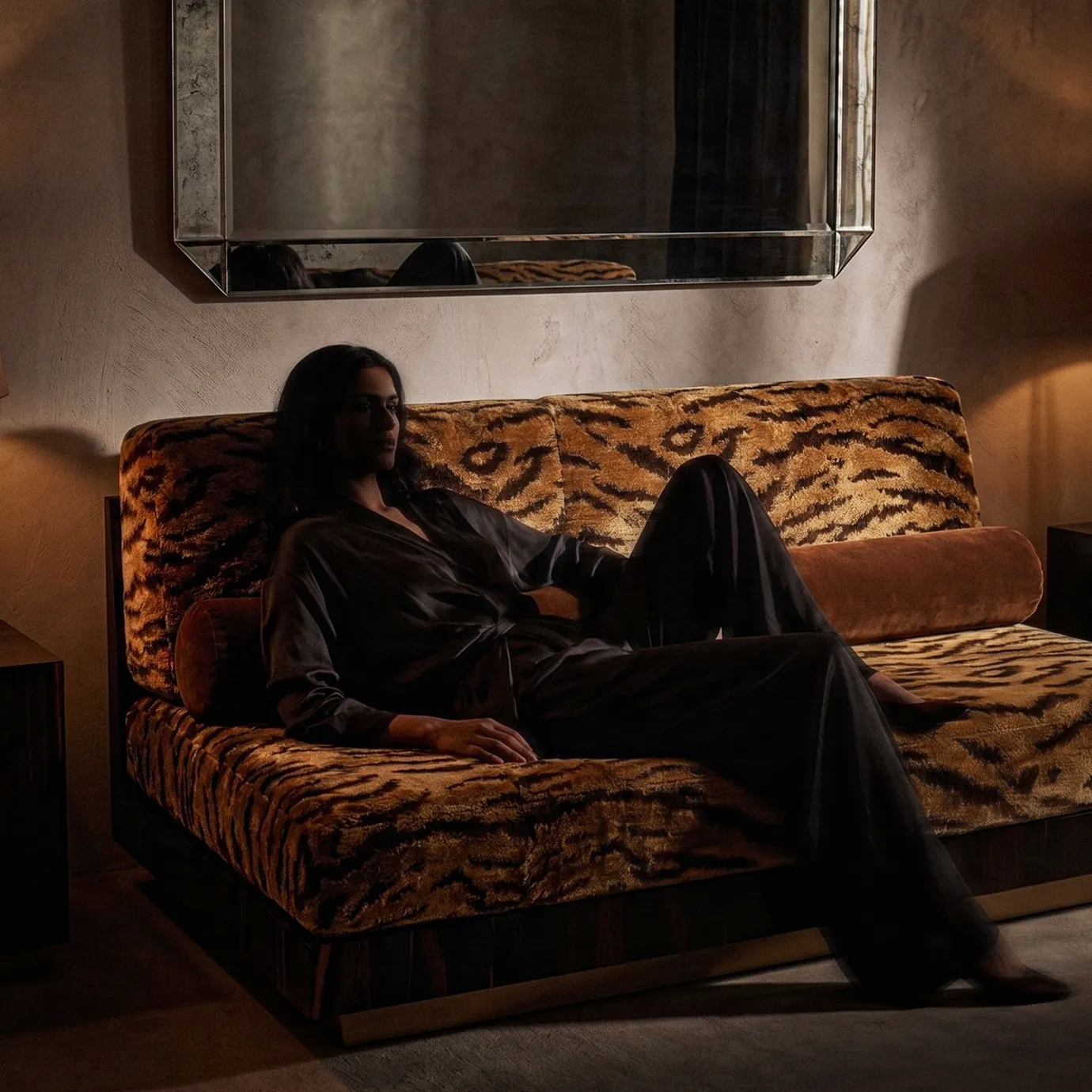 Eileen modular sofa by KOKET in a dark interior with a person reclining on the tiger-print velvet, a bevelled mirror above.
