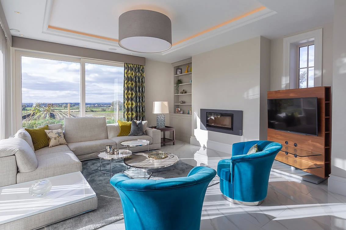 Bright Broughshane living room with two Countess Chairs, facing a modern fireplace and scenic window views.