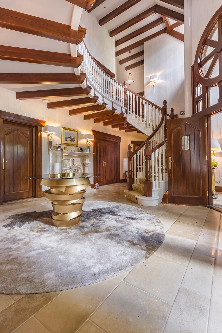 Country Down showcases a grand English manor foyer with a sweeping staircase and the elegant Intuition Dining Table.