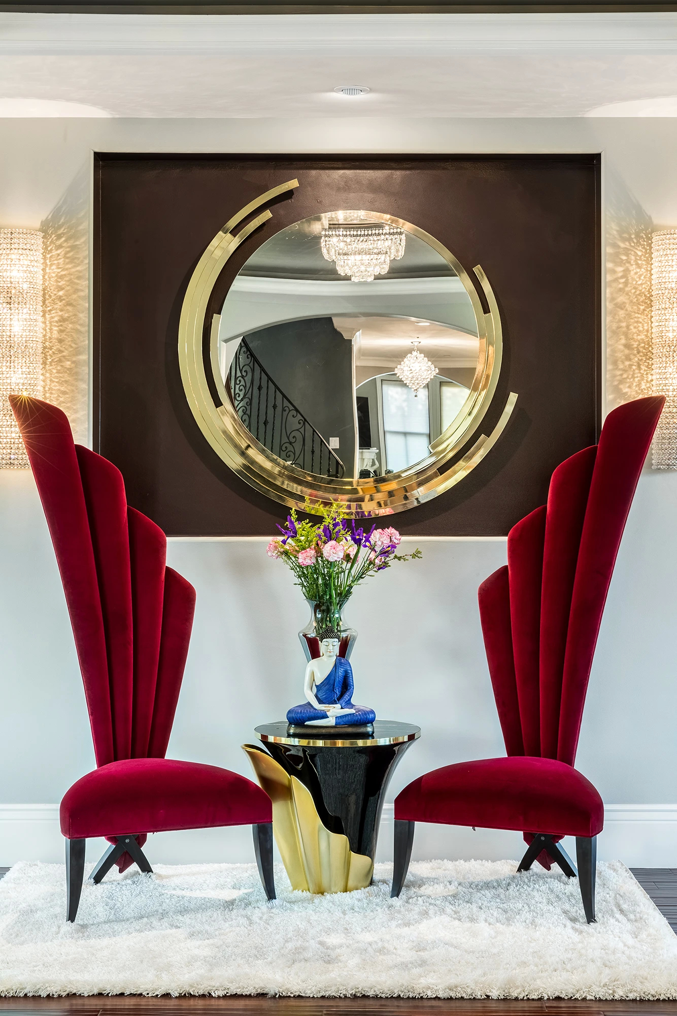 Mission Hills Residence features the Yasmine Side Table flanked by two striking red velvet chairs, beneath a circular gold mirror.