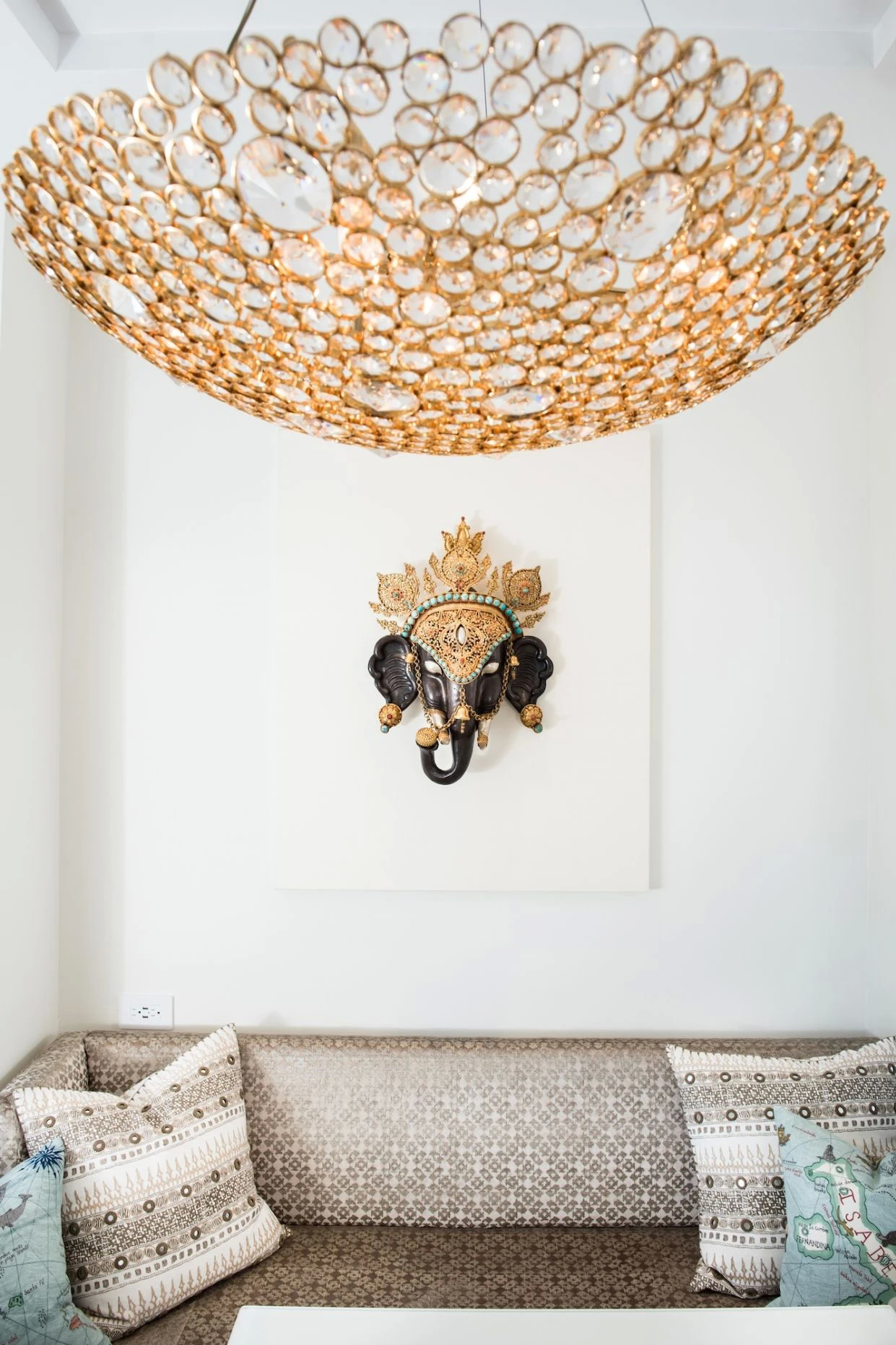 Koket's Apartment In New York: a Kasehsiah Chandelier hangs above a couch and a Ganesha metal wall hanging.
