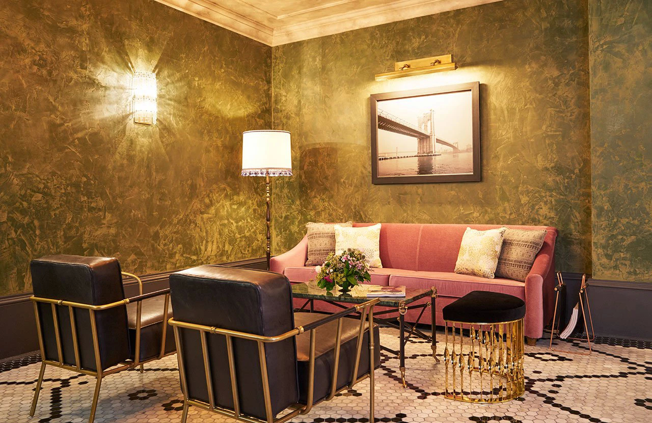 Koket's Beekman Hotel: a chic lounge with a pink sofa, chairs, and a gold Mandy Stool on a mosaic floor.