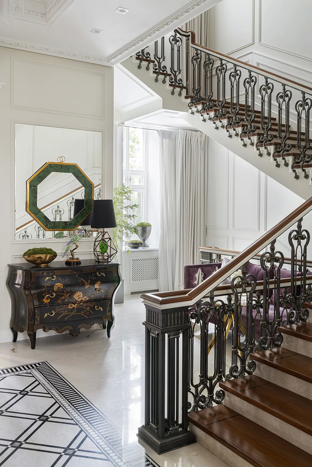 A classic entrance hall with a staircase, mirror, and a black and gold chest, part of Koket's Holiday Interior.