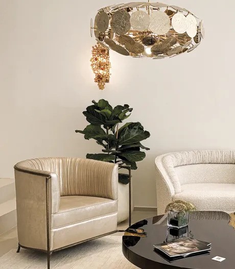 A stylish living room featuring a beige Desire Chair next to a large plant. Above, two unique light fixtures hang.