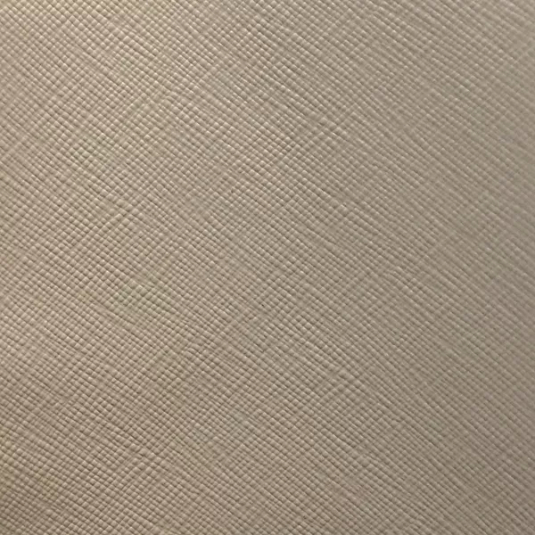 A detailed view of Nomad Synthetic Leather in a light, neutral tone shows a fine, diagonal cross-hatch texture across the surface.