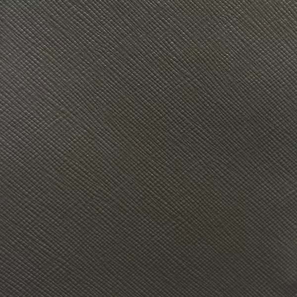 A close-up of Nomad Synthetic Leather in a deep charcoal gray reveals a fine, diagonal cross-hatch texture across the surface.