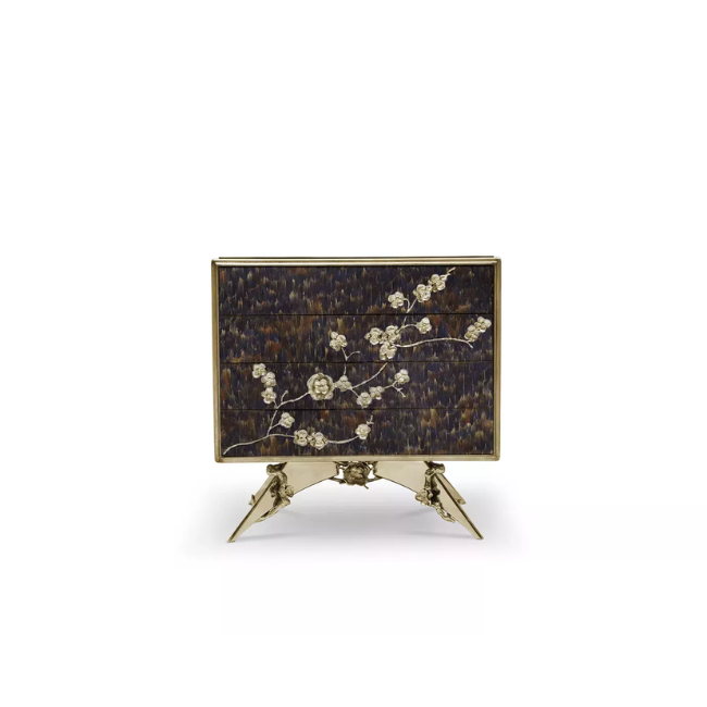 The Spellbound Peacock Purple Feather Nightstand’s structure is adorned with purple feathers ornamented with elegant golden flower-shaped details along the front of the four drawers.